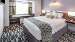 A hotel room with a large bed, bedside tables, a window with curtains, a flat-screen TV, and a wall-mounted light fixture. - Microtel Inn by Wyndham Victor/Rochester (Victor)