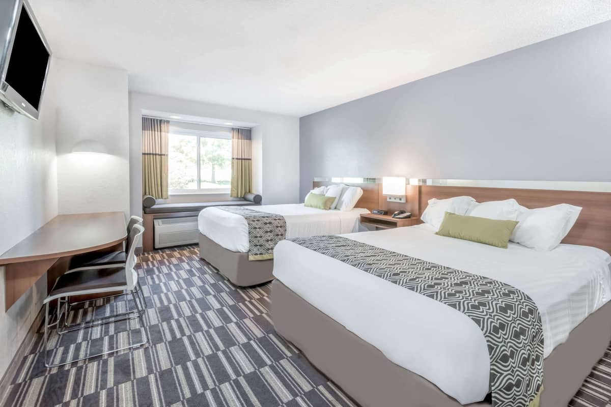 A hotel room with two beds, a desk, a chair, a TV, and a window with curtains.