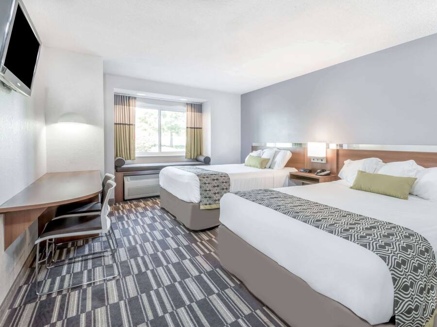 A hotel room with two beds, a desk, a chair, a TV, and a window with curtains.