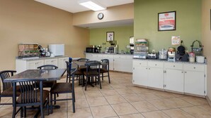 A clean, well-lit kitchen area with a dining table and chairs, equipped with various appliances and a clock on the wall. - Econo Lodge Belton - Kansas City South (Belton)
