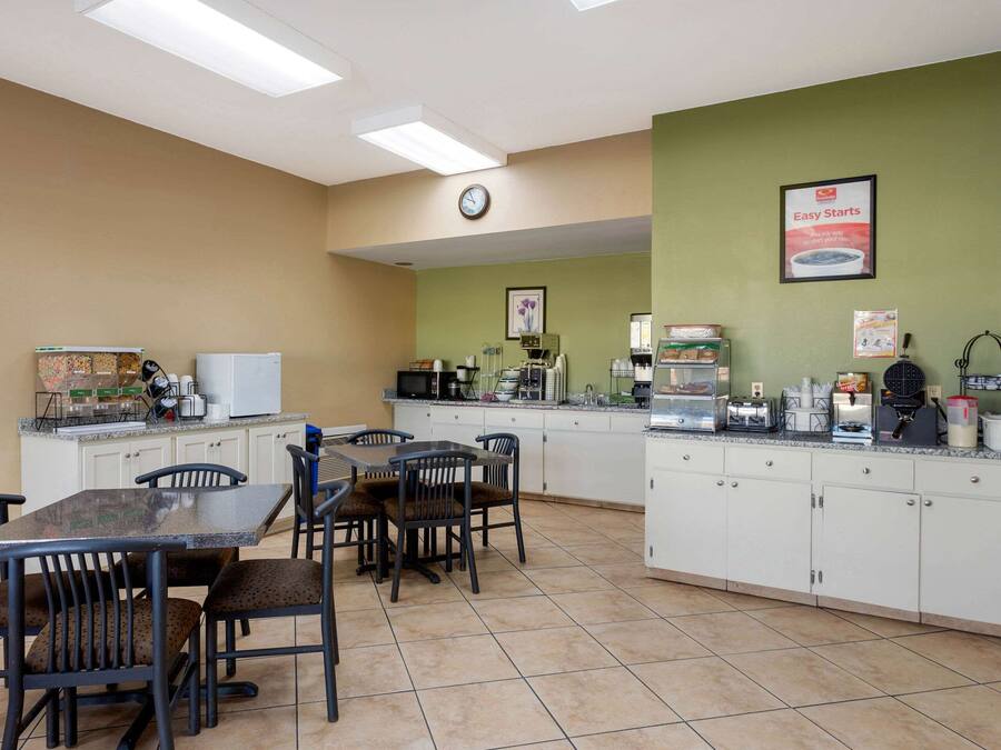 Un'area cucina pulita e ben illuminata, con un tavolo da pranzo e sedie, dotata di diversi elettrodomestici e una sveglia appesa al muro.