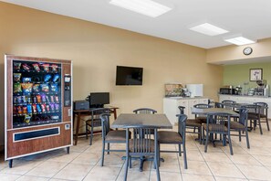A dining area with a vending machine, a television, and a kitchen area. - Econo Lodge Belton - Kansas City South (Belton)