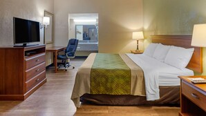 A hotel room with a bed, a desk with a chair, a television, and a lamp. - Econo Lodge Belton - Kansas City South (Belton)