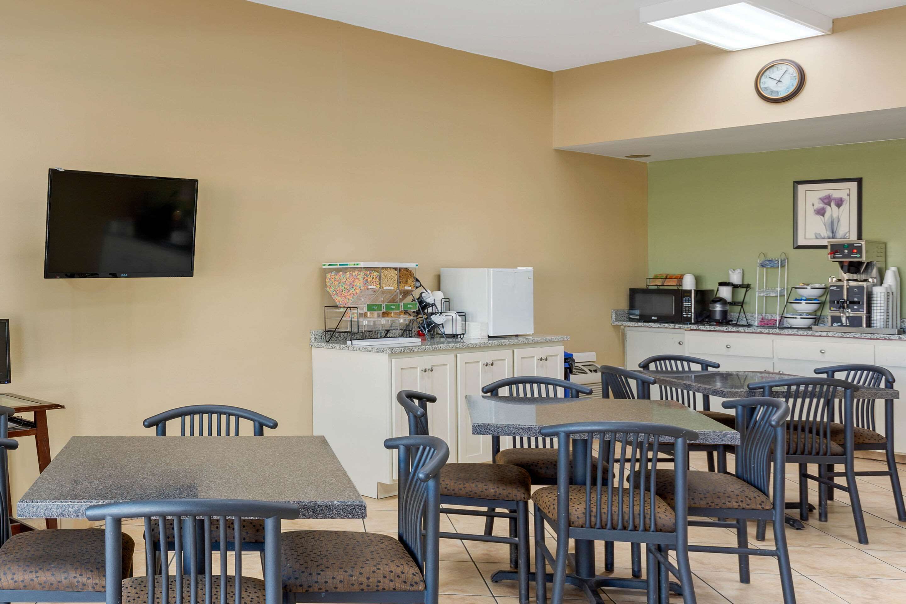 A dining area with tables and chairs, a flat-screen TV mounted on the wall, a refrigerator, and a microwave on the counter.