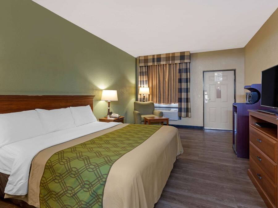 Una habitación de hotel con cama, escritorio, silla, televisor y puerta.