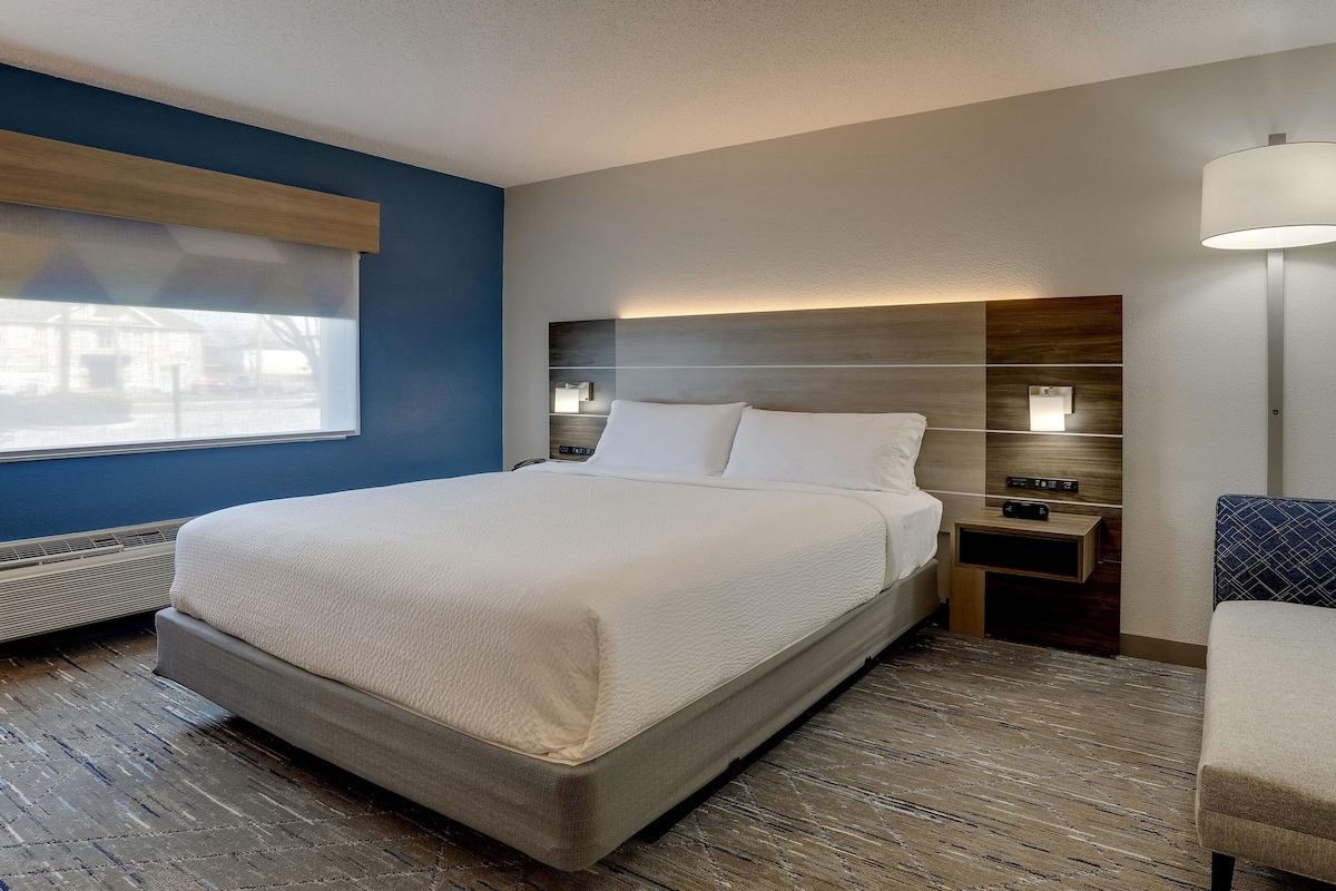 A hotel room with a bed, bedside table, lamp, and a chair.
