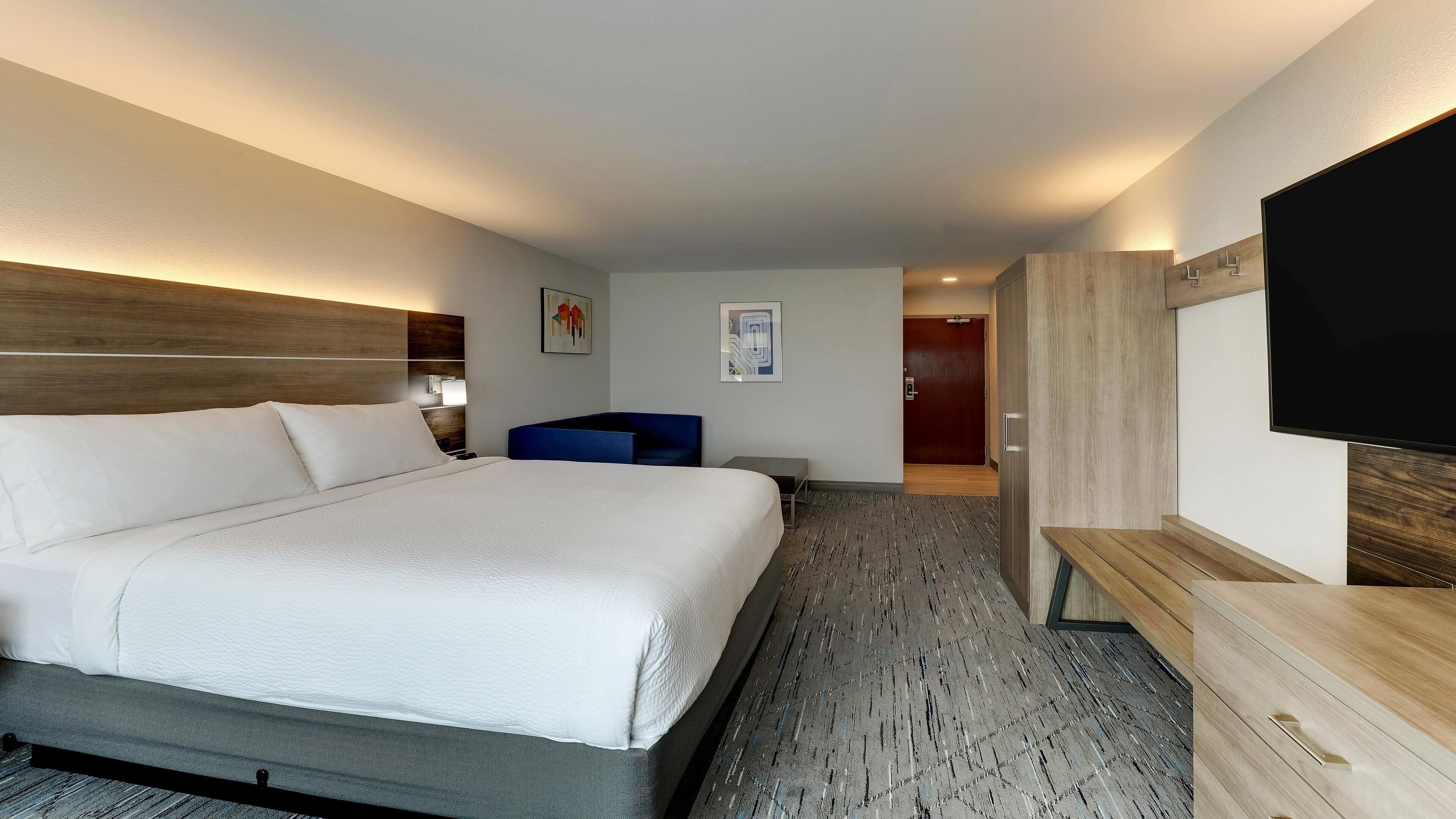 A hotel room with a large bed, a desk, a chair, a TV, and a door leading to a bathroom.