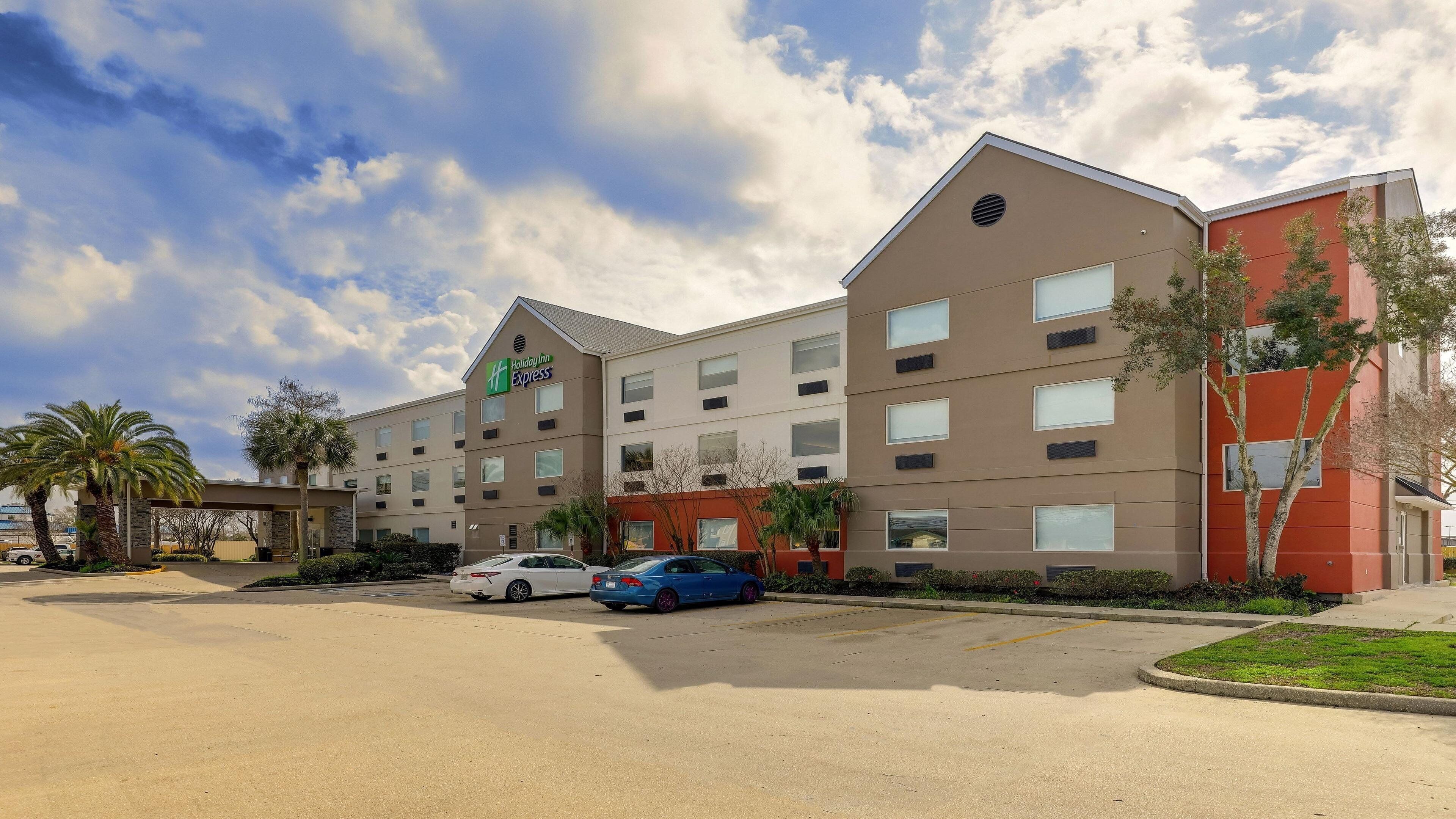 Un hotel Holiday Inn Express con estacionamiento, varios coches y palmeras.