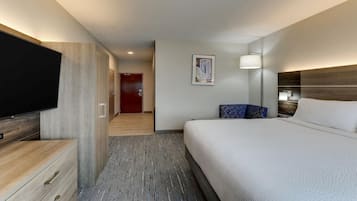 A hotel room with a bed, a TV, a desk, and a door leading to a hallway.