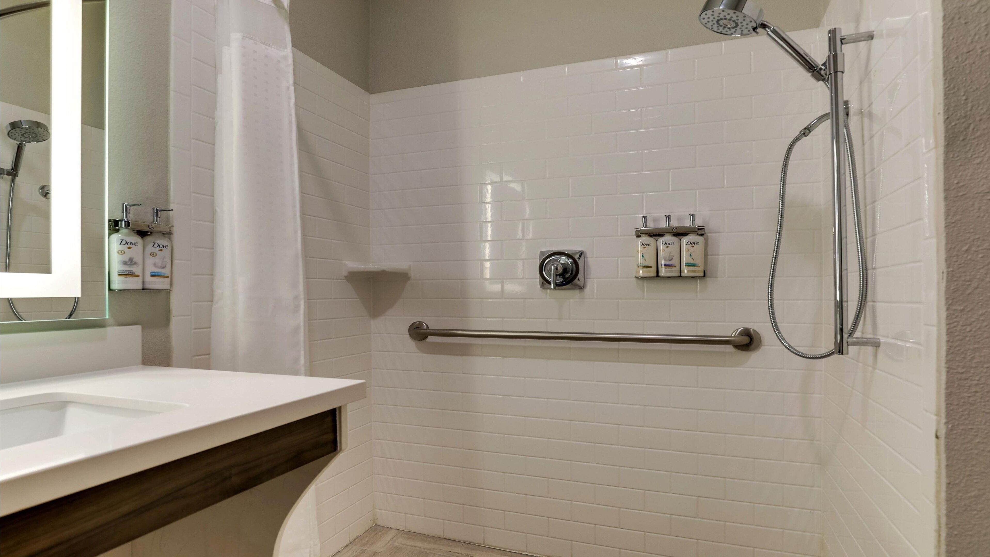A bathroom with a white sink, a shower with a handheld showerhead, and a towel rack with three bottles of Dove soap.