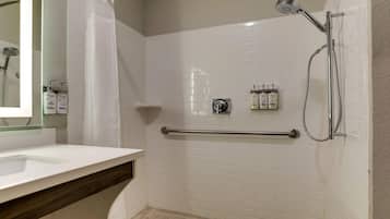 A bathroom with a white sink, a shower with a handheld showerhead, and a towel rack with three bottles of Dove soap.