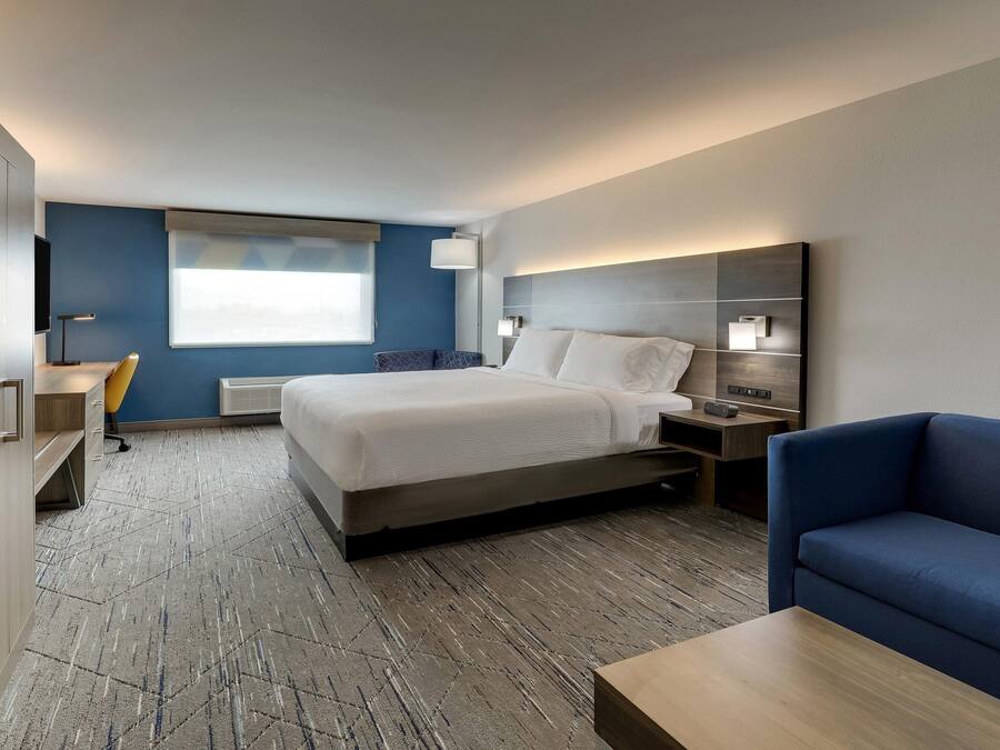 A modern hotel room with a bed, bedside table, lamp, and a blue sofa.