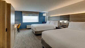 A hotel room with two beds, a desk, a chair, a window with blinds, and a nightstand with a lamp.