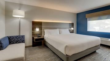 A hotel room with a large bed, a bedside table with a lamp, a nightstand, and a wall-mounted control panel.