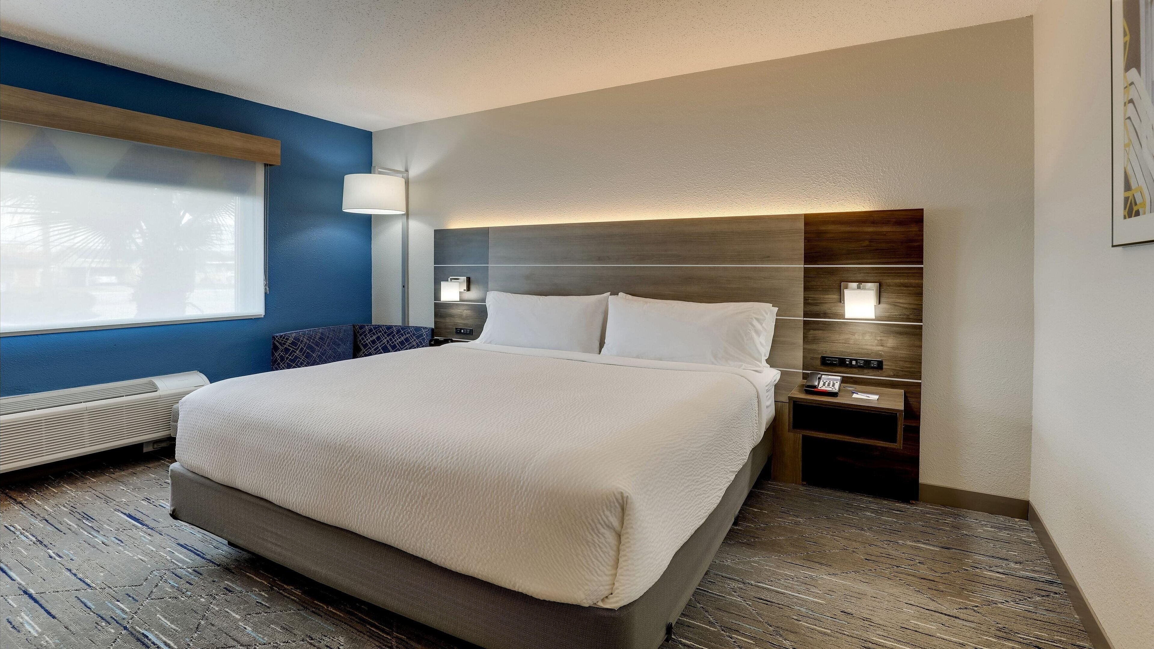 Habitación de hotel con una cama grande, una mesita de noche con lámpara, un calentador y vistas al exterior.