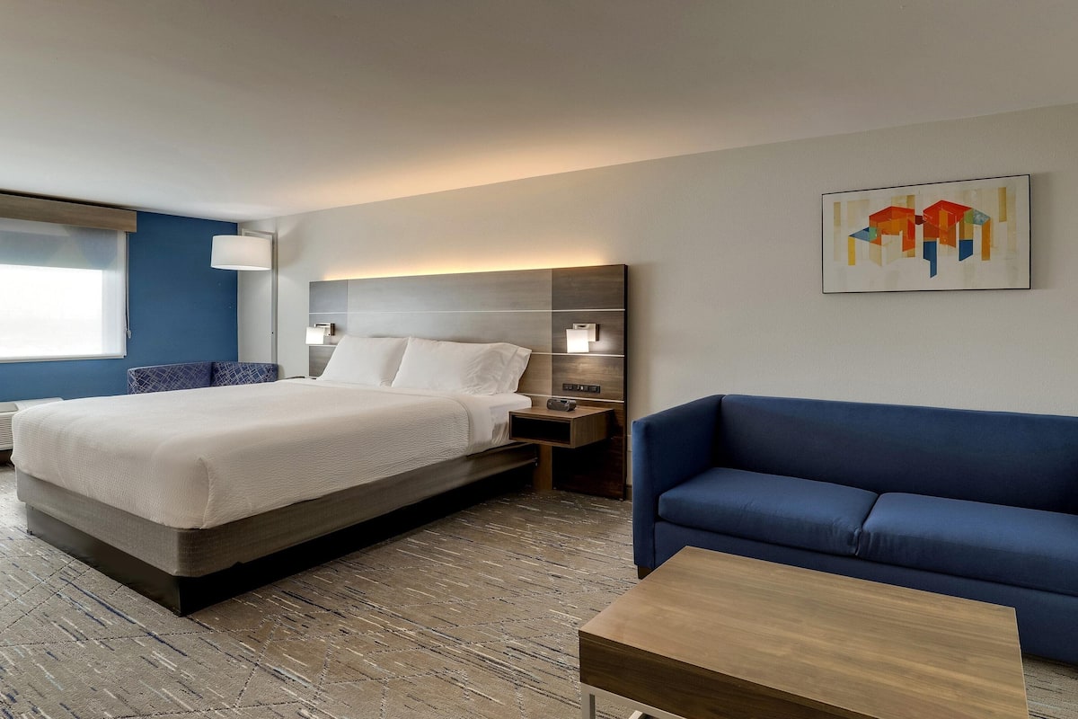 A hotel room with a large bed, a blue sofa, a wooden coffee table, and a wall-mounted artwork.