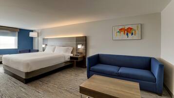 A hotel room with a large bed, a blue sofa, a wooden coffee table, and a wall-mounted artwork.
