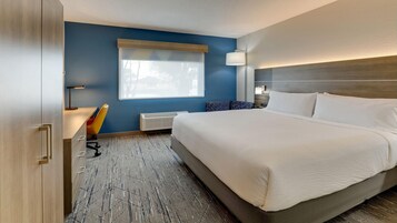 Habitación de hotel con una cama grande, un escritorio con silla, una ventana con persianas, una lámpara de pared y un radiador.