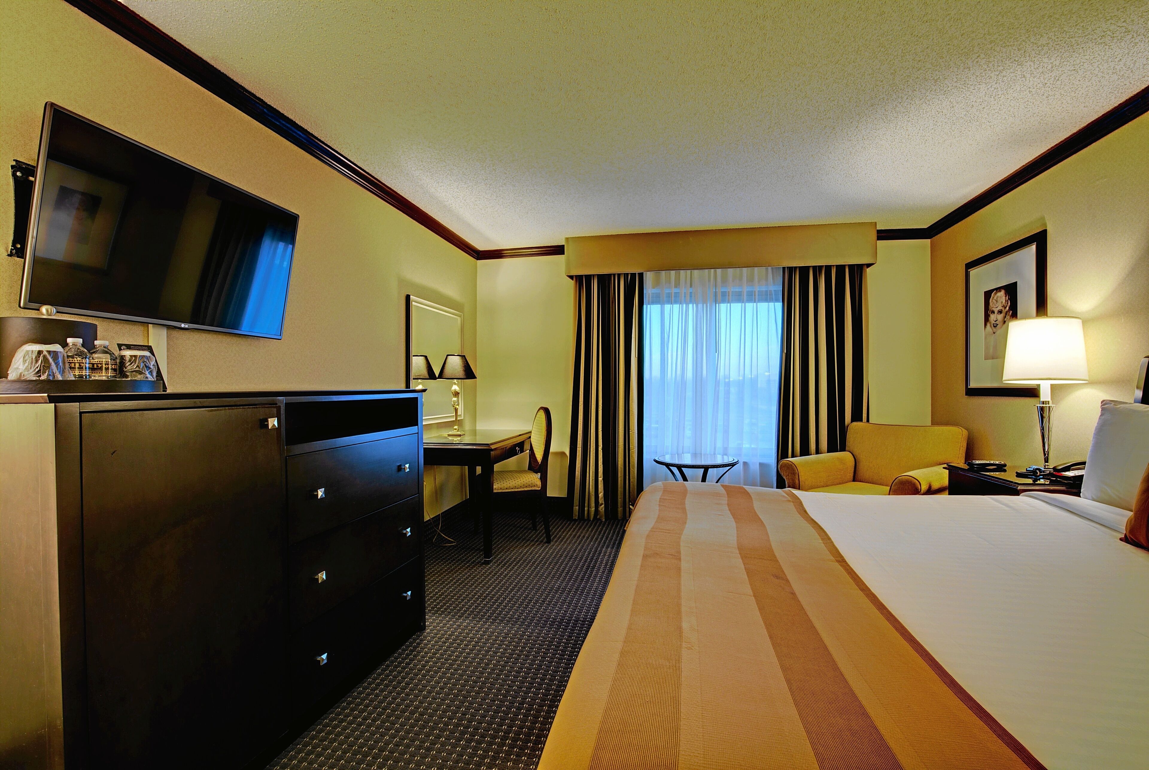 A hotel room with a bed, a desk, a chair, a television, and a dresser.