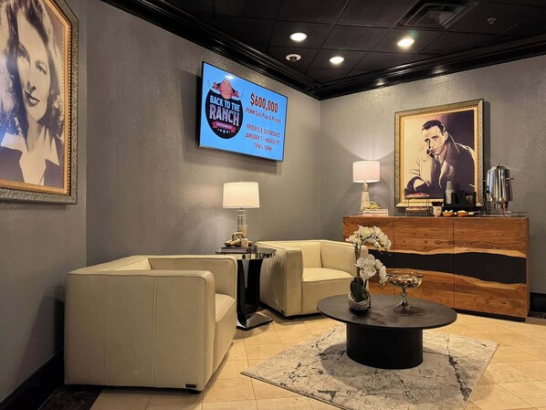 Un hall con un televisor mostrando un premio de 600.000 dólares, un mostrador de recepción, dos sofás, una mesa de centro y un retrato enmarcado.