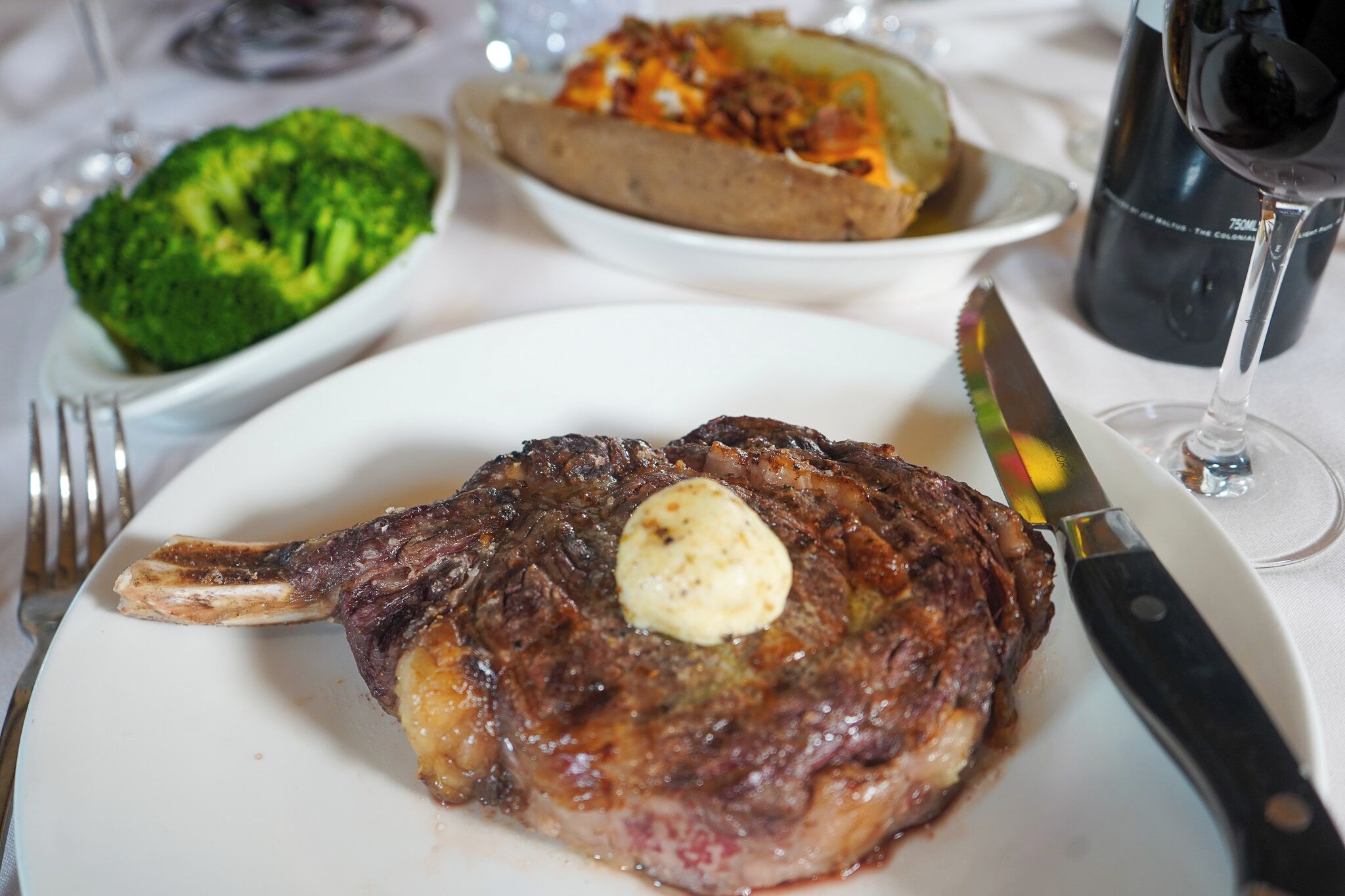 Bife com um pouco de manteiga em um prato branco, acompanhado de garfo e faca sobre a mesa.