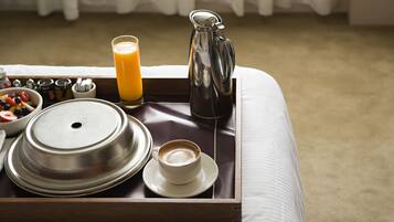 A breakfast tray with a coffee cup, a glass of orange juice, a pitcher, and a bowl of fruit on a bed.