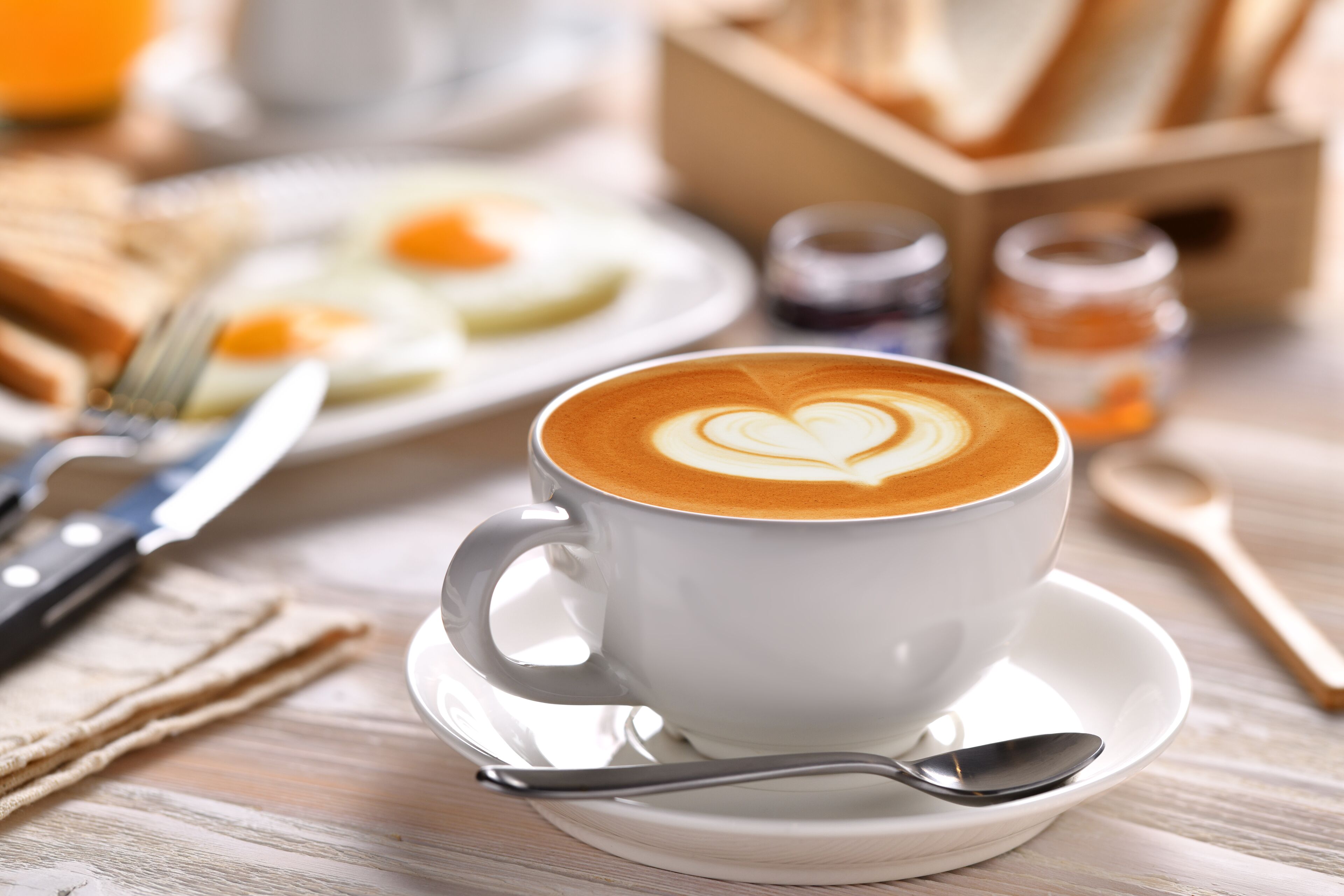 A cup of coffee with latte art on a saucer, a spoon, a fork, and a napkin on a wooden table.