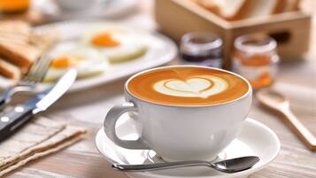 A cup of coffee with latte art on a saucer, a spoon, a fork, and a napkin on a wooden table.