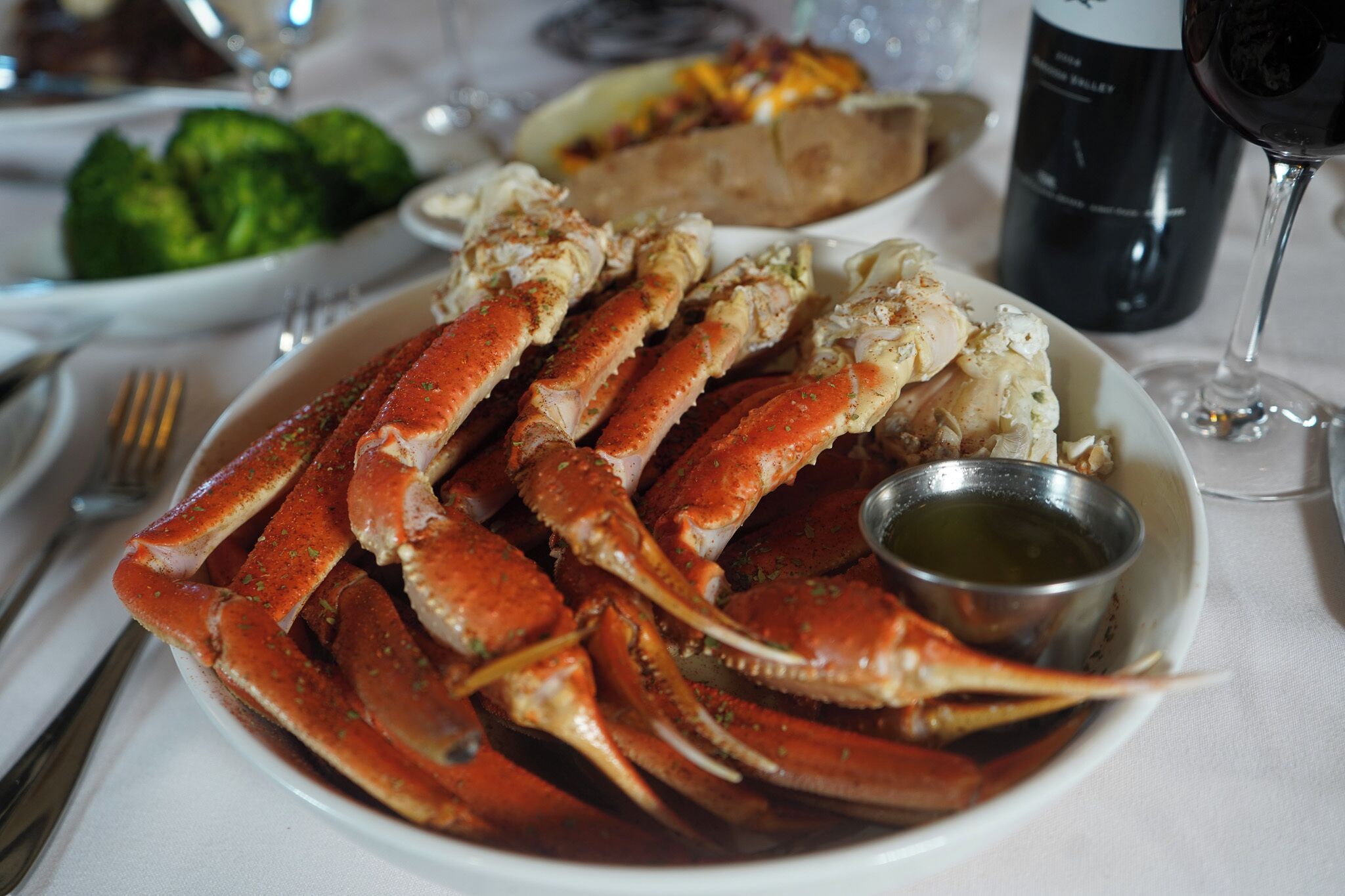 Plat de gambes cuites amb un bol petit de salsa, una ampolla de vi i un got de vi damunt d'una taula.