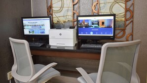 Dos computadoras de escritorio HP sobre un escritorio con dos sillas de oficina blancas, una impresora y decoración en la pared.