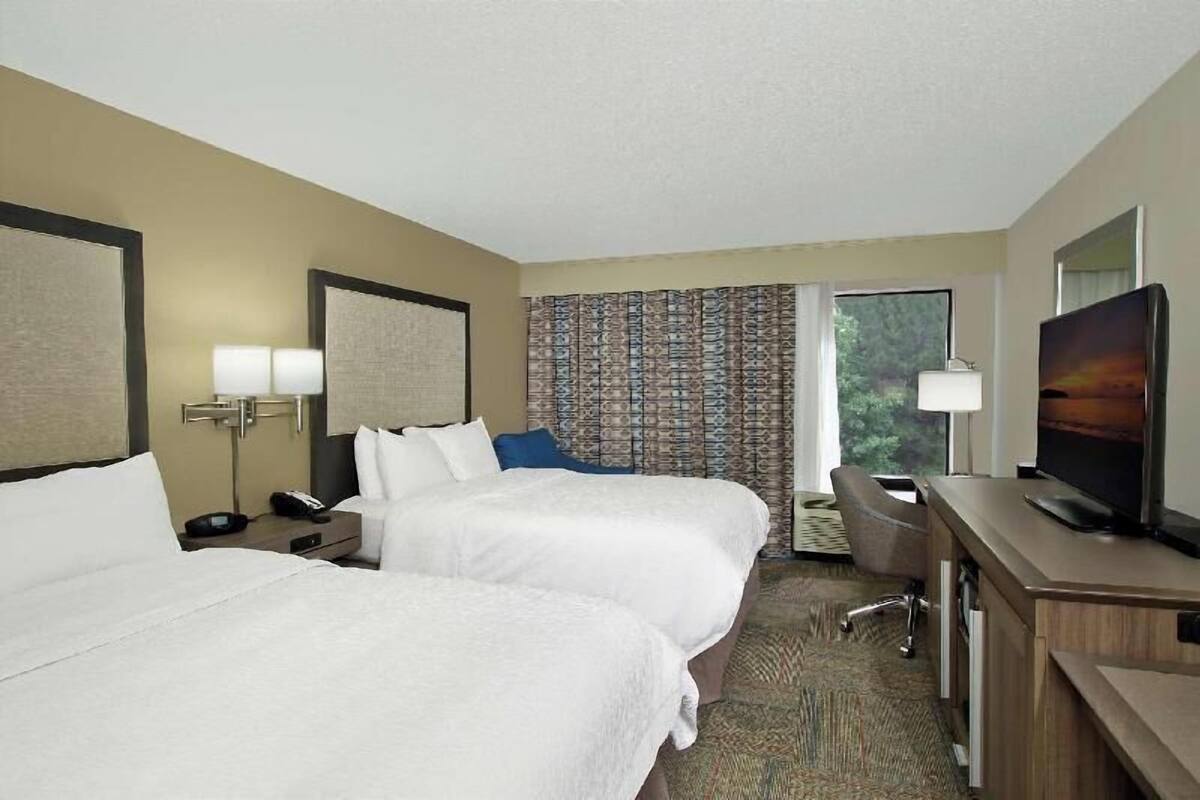 A hotel room with two beds, a desk with a TV, a lamp, and a patterned curtain.
