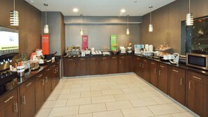 Una cocina moderna con armarios de madera, piso de baldosas y diversos alimentos para el desayuno sobre la encimera.