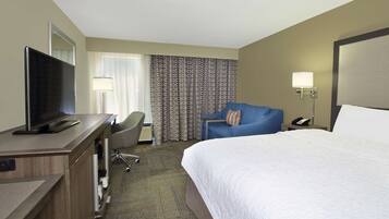 A hotel room with a bed, a desk with a TV, a chair, a lamp, and a phone on a side table.