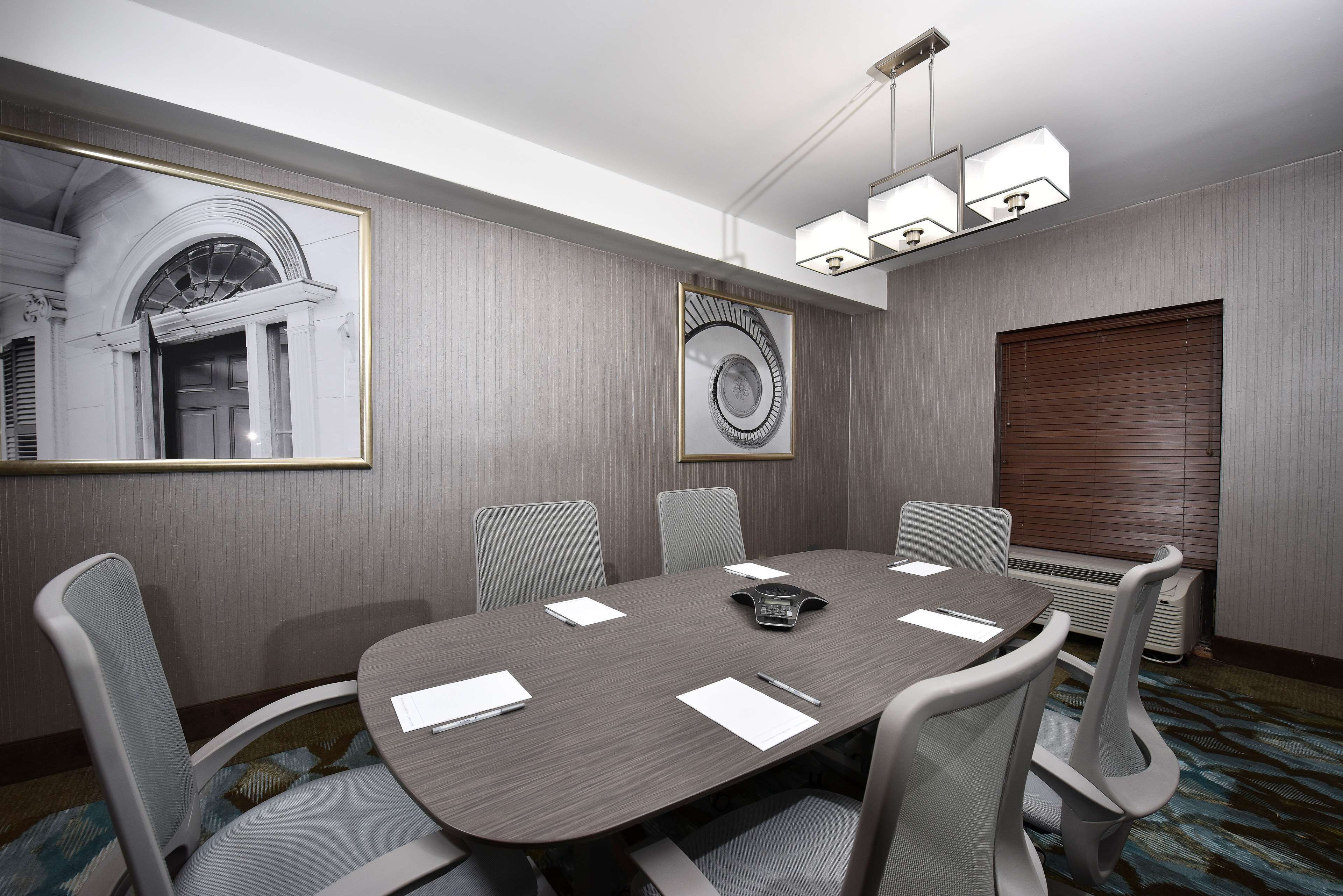 A conference room with a long table, six chairs, a telephone, and a framed artwork on the wall.