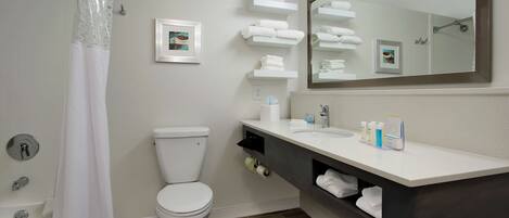 A modern bathroom with a white toilet, a shower with a white curtain, a large mirror, and a vanity with a dark cabinet.