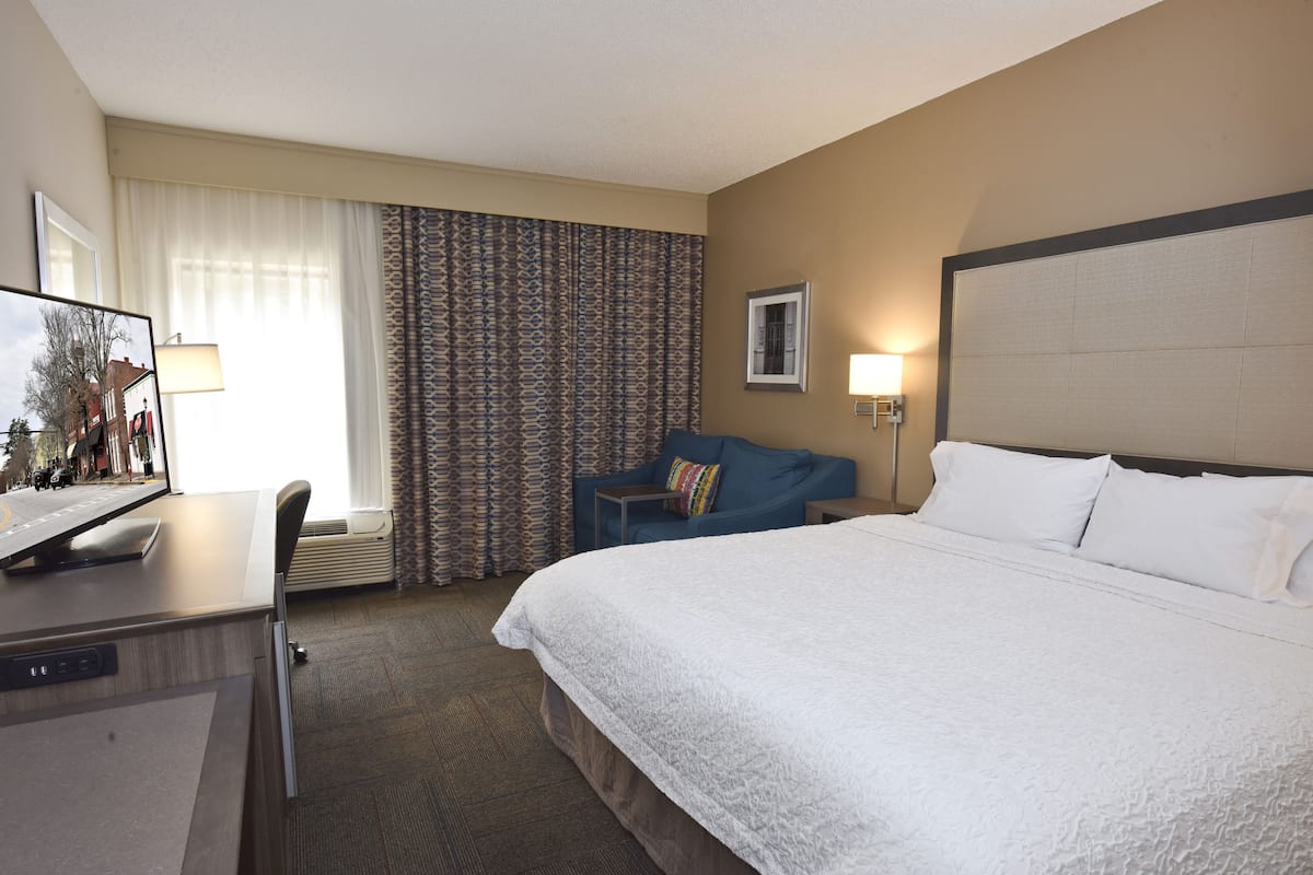 A hotel room with a large bed, a desk with a computer, a chair, a TV, and a window with curtains.