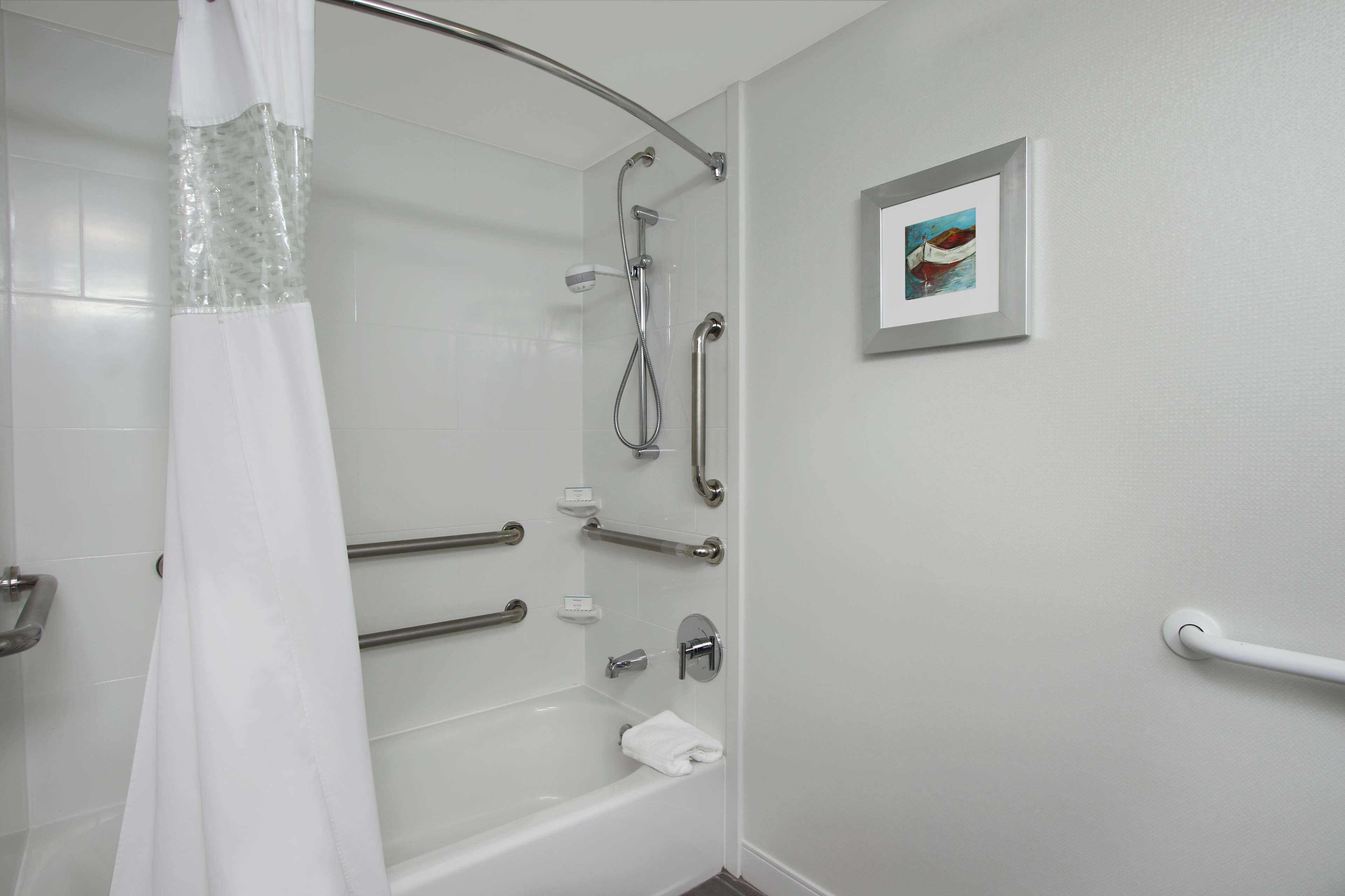 Un bagno moderno con doccia a pavimento, maniglie di sostegno e un quadro appeso al muro.