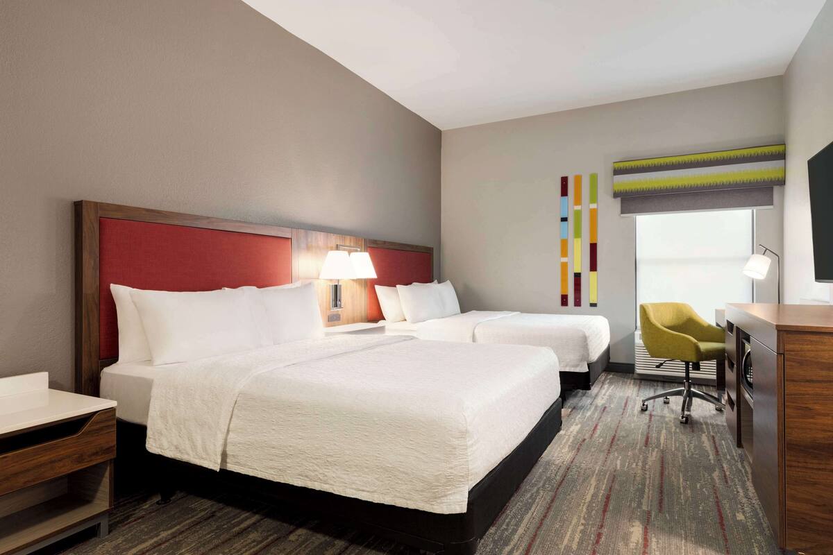 A hotel room with two beds, a desk, a chair, a TV, and a window with a view.