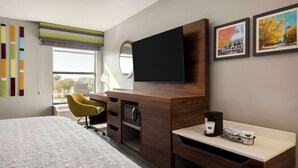 A modern hotel room with a large bed, a desk with a coffee maker, a TV, and a window with a view of trees. - Hampton Inn Starkville Mississippi State University (Starkville)
