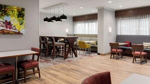 A modern hotel lobby with a dining area, seating, and a large window with curtains. - Hampton Inn Starkville Mississippi State University (Starkville)