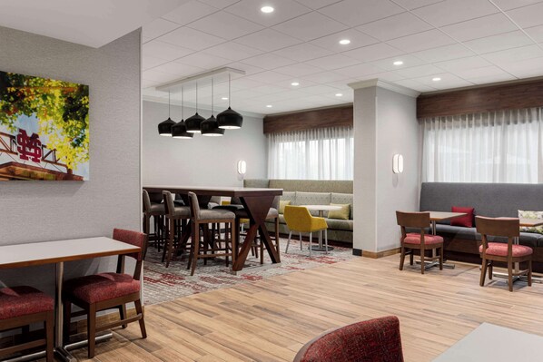A modern hotel lobby with a dining area, seating, and a large window with curtains.