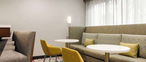 Een hotelkamer met een bank, twee gele stoelen, een klein rond tafeltje en een spiegel aan de muur.