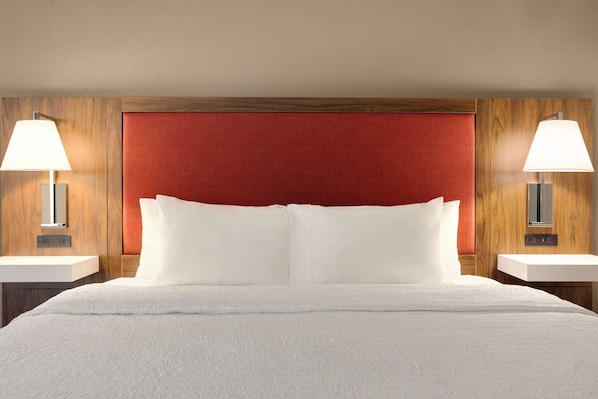 A hotel room with a large bed, two bedside tables with lamps, a wooden headboard, and a red accent wall.