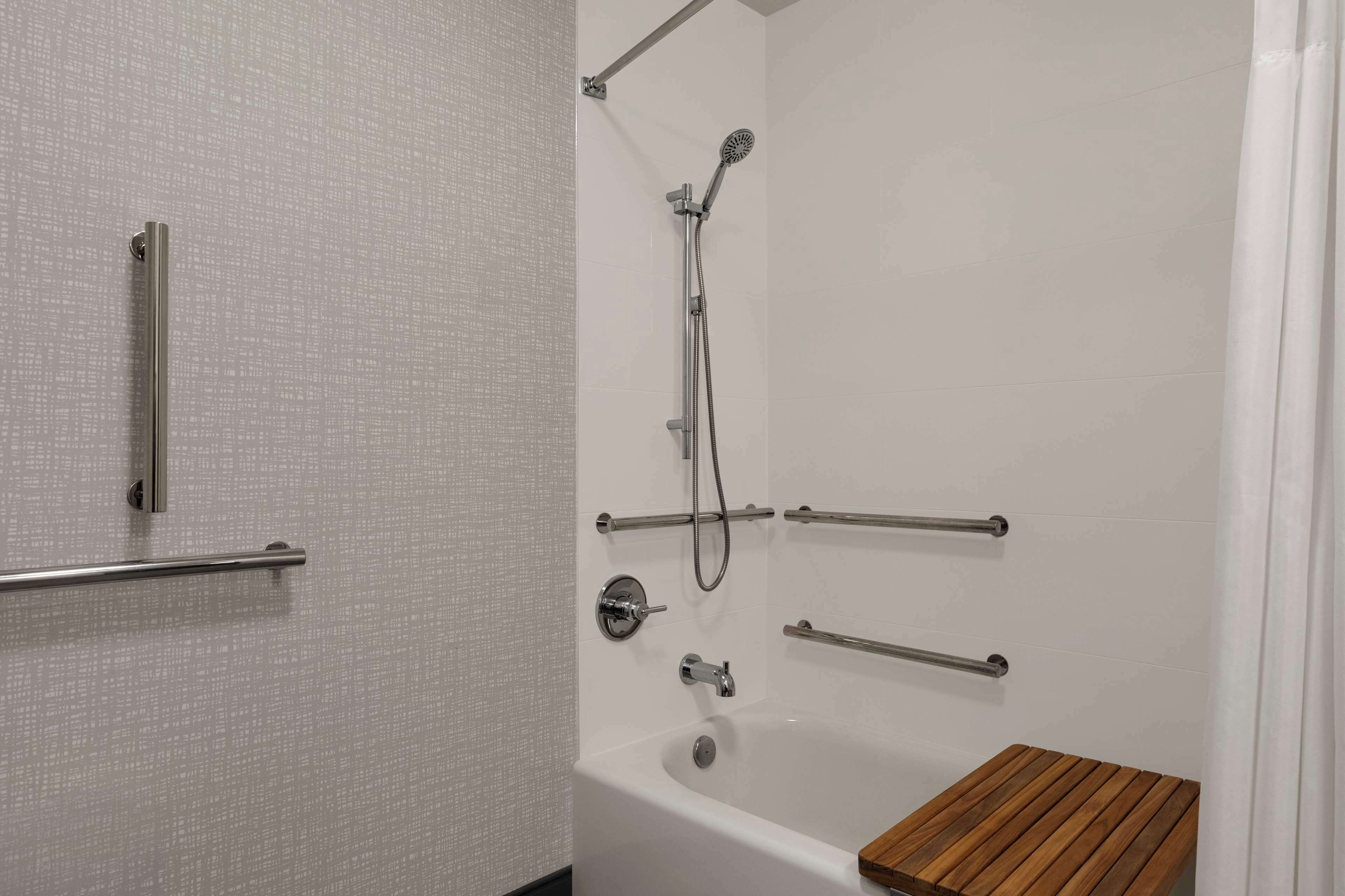 Une salle de bain moderne avec une baignoire blanche, un banc en bois et plusieurs barres d’appui pour plus de sécurité.