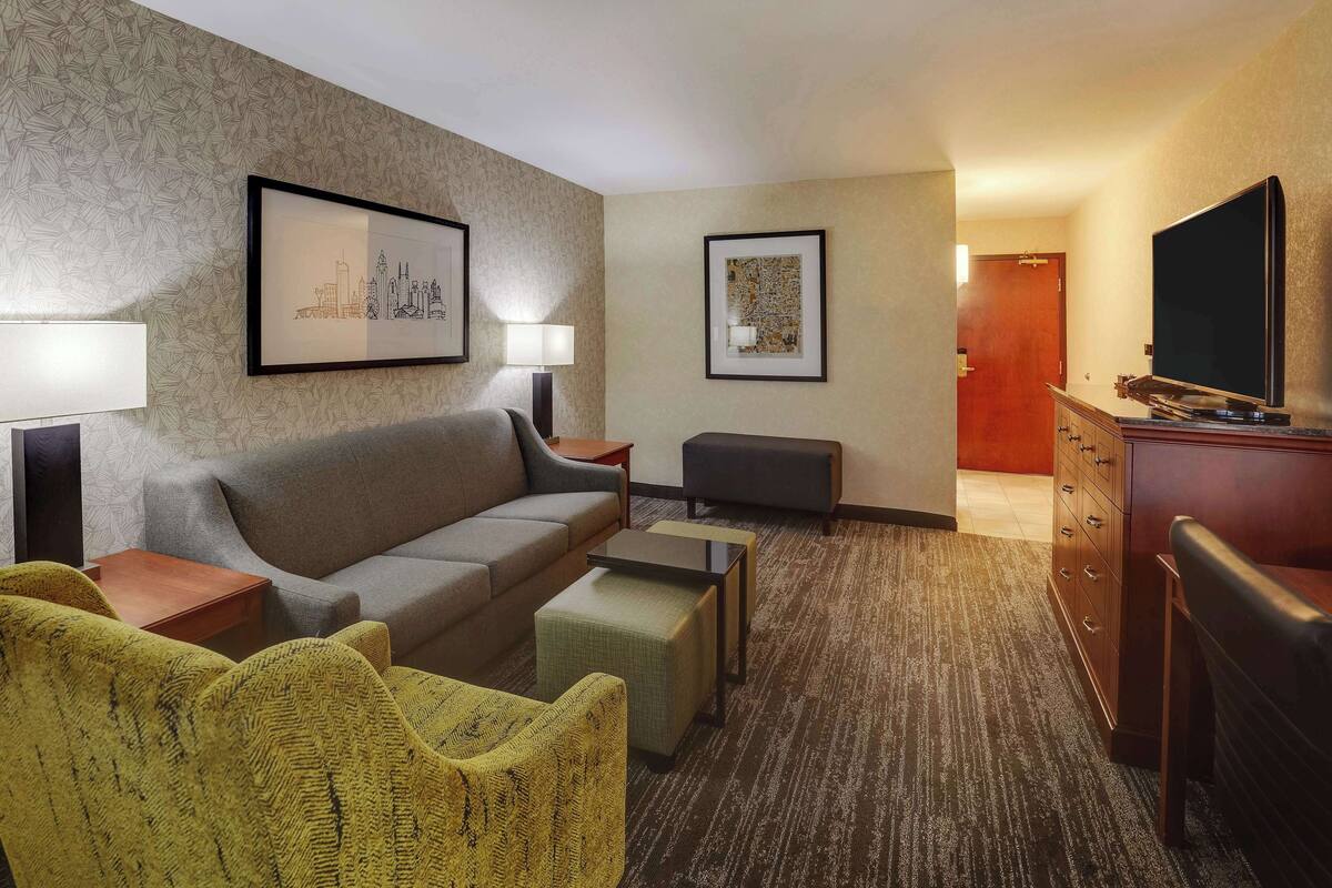 A hotel room with a sofa, armchairs, a coffee table, a TV, and a dresser.