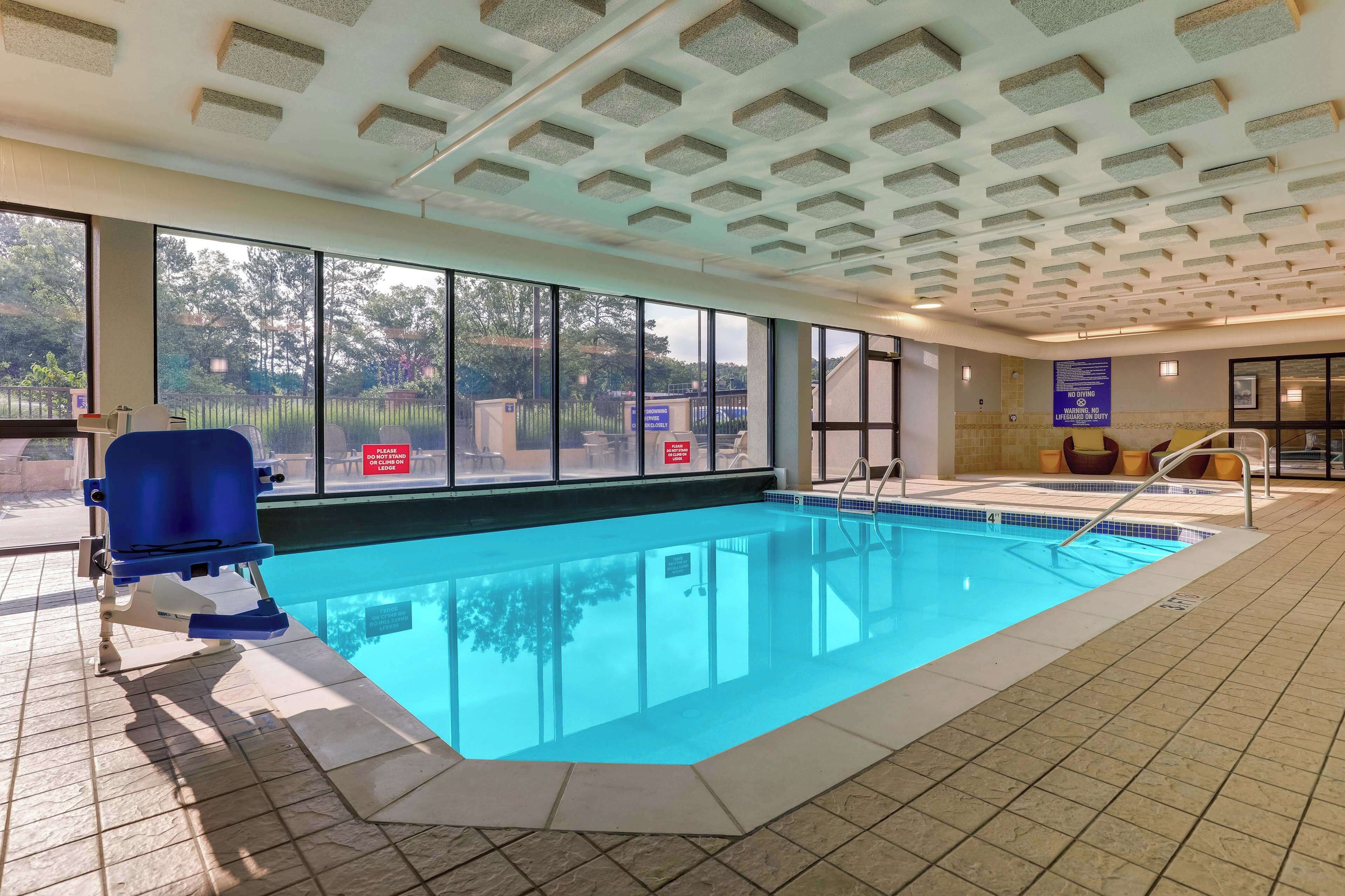 Una piscina interior con paredes de vidrio transparente, suelo de baldosas y techo con un diseño geométrico.