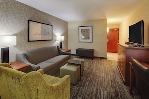 Una habitación de hotel con sofá, sillón, mesa de centro y televisor.