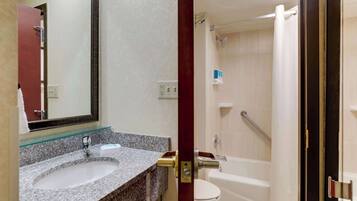 Un baño con lavamanos de encimera de granito, un espejo, inodoro y zona de ducha.