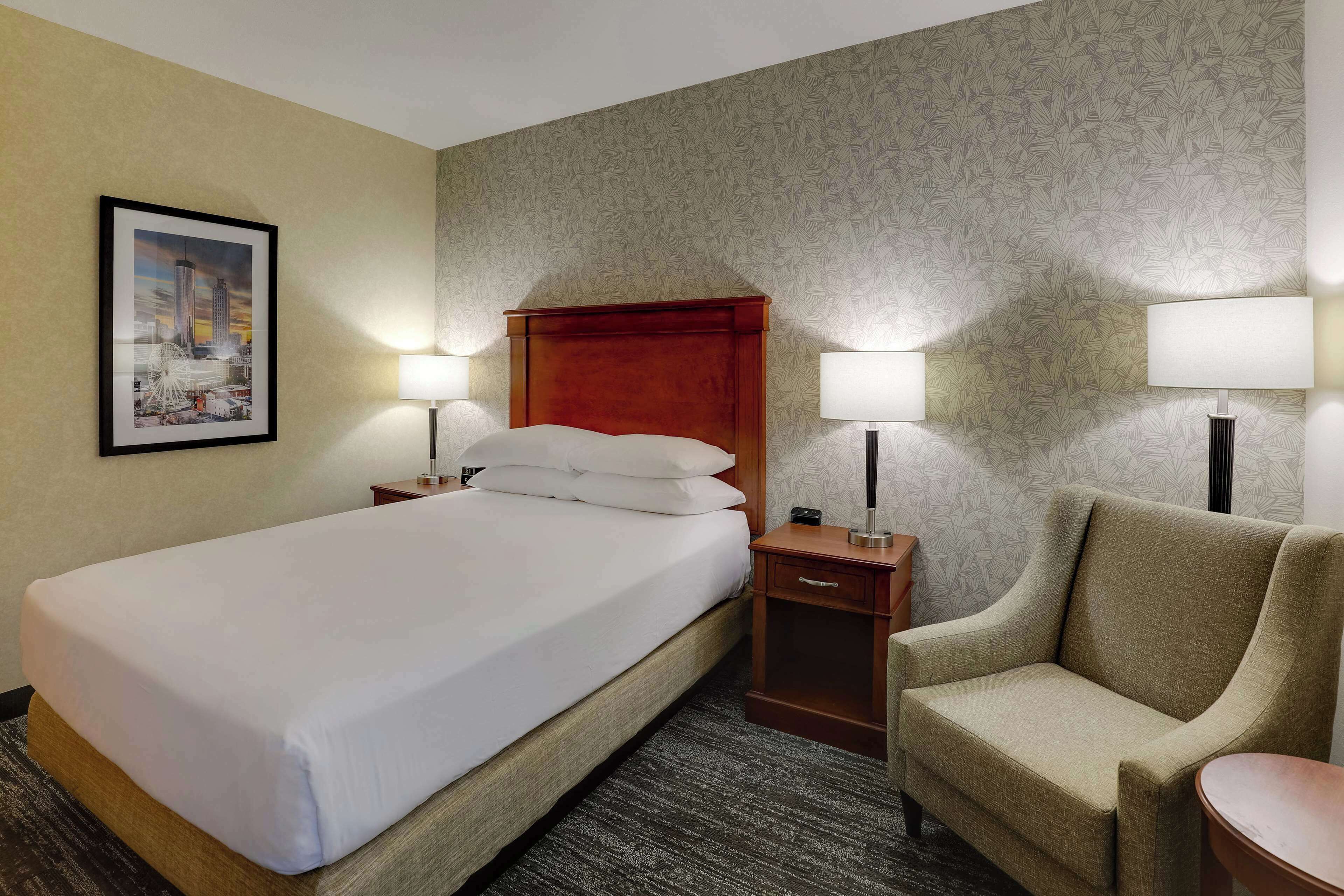 A hotel room with a bed, two bedside tables, a chair, and a lamp.