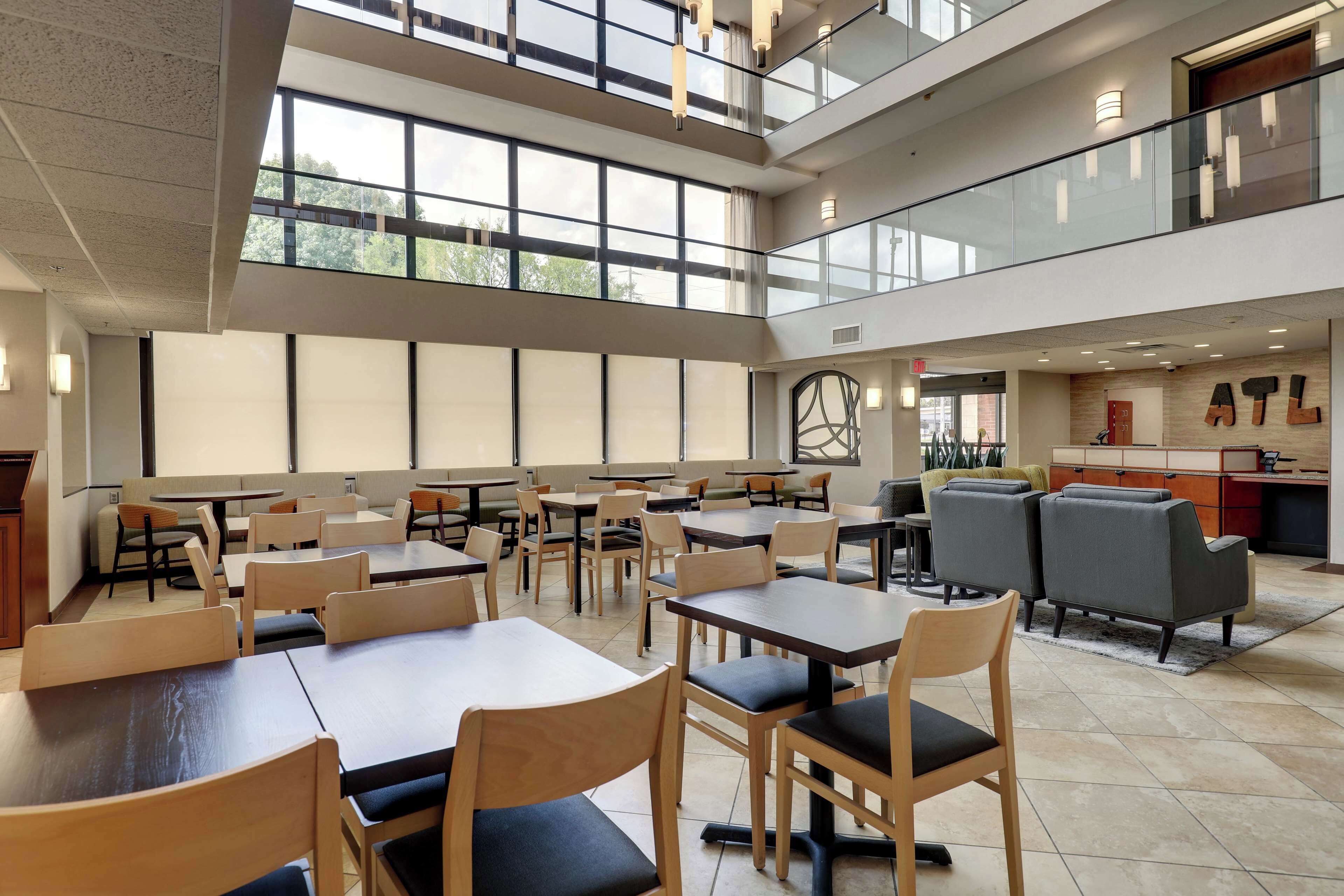 A spacious indoor area with multiple seating arrangements, including tables and chairs, and a large window providing natural light.
